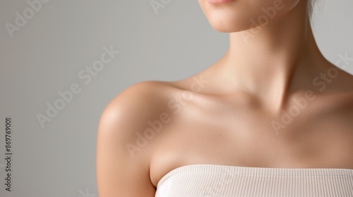 Close-up of a woman's shoulder and collarbone area, highlighting smooth, radiant skin in a soft, neutral background.