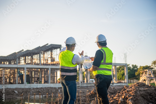 Two Architect man discussing about the building plan and see how the construction progressive at the construction site