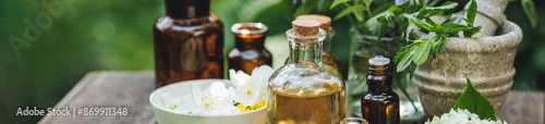 Concept of alternative herbal medicine. Bottles of tincture or potion, organic essential oils, healthy herbs, floral extracts on wooden table. Pure natural ingredients for cosmetic production banner