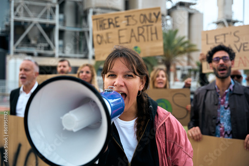 Close up portrait nonconformist gen z activist woman shouting at protest holding megaphone to group of people at a demonstration against pollution and factories with banners of climate change messages