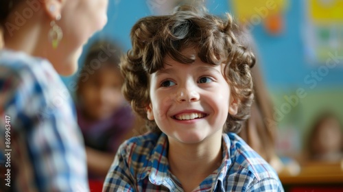 A young boy with curly hair is smiling in a classroom setting, interacting with his classmates, creating a cheerful and engaging learning environment.