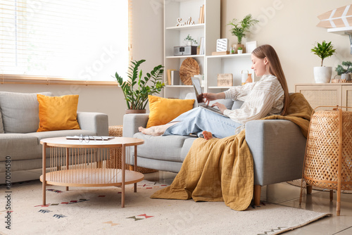 Beautiful young woman using laptop and relaxing on sofa in living room