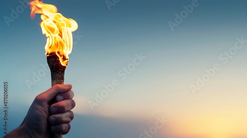 Hand holding a burning torch against a clear evening sky, symbolizing hope, leadership, achievement, and the sportspirit.