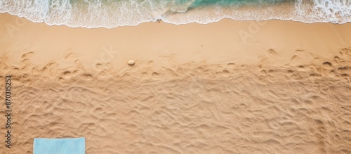 Sandy beach seen from above with towel border, summer accessories, and visible sand texture, creating a background with copy space image on the left side.