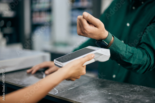 A female hand holding a payment machine and a male paying over his smartwatch.