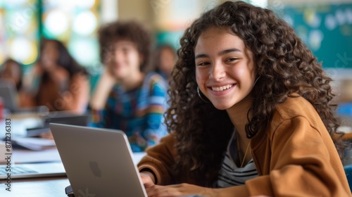 A photograph of a smiling student sitting in a classroom using a laptop, representing education, learning, and youthful enthusiasm in a bright and engaging school environment.