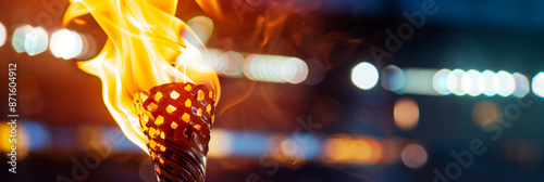 Close-up of a burning olympic torch with a flame against a blurred stadium with bokeh at night