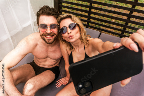 Young couple of vacationists in sunglasses photographing themselves with the smartphone camera during outdoor recreation. Leisure and summer vacation concept