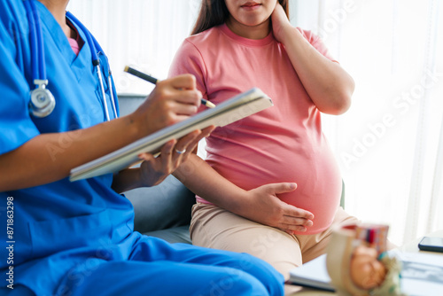 Asian female doctor and nurse consult on sofa with a pregnant woman, using ultrasound and stethoscope, addressing illnesses morning sickness, gestational diabetes, hypertension, ensuring her health.