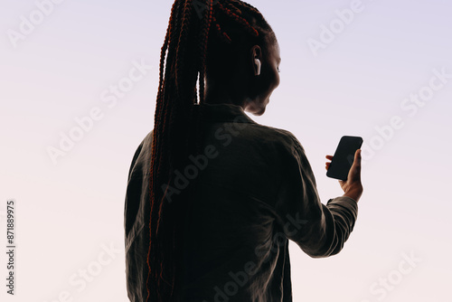 Happy young woman smiling while making a video chat on her smartphone, studio silhouette