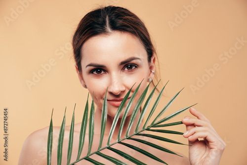 Beauty portrait of amazing gorgeous beautiful brunette woman. Smiling model posing naked. Female isolated over beige wall background with green nature leaf plant. Cheerful and happy
