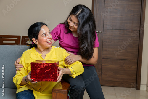 indian Daughter giving gift to mother on Mothers day , Daughter and mother bonding sitting on sofa at living room.