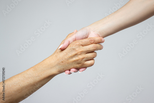 The hand of a young girl holds the hand of an elderly woman, isolated on a light gray background. The concept of caring for retired parents. Helping hand. Support for people with aging diseases