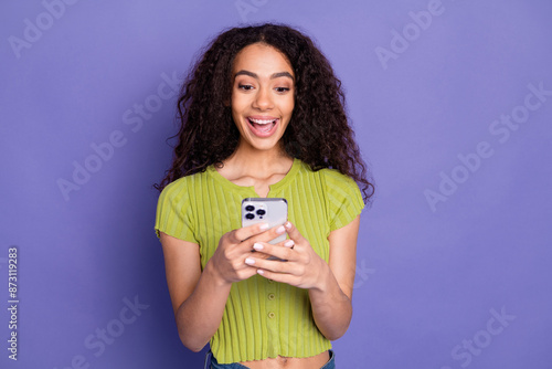 Photo portrait of attractive teen woman hold device excited dressed stylish green clothes isolated on purple color background