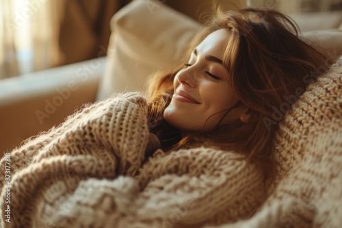 A serene woman rests on a couch, wrapped in a cozy knit sweater. Her eyes are closed, with a gentle smile conveying contentment and relaxation.