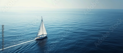 A sailboat with white sails navigates the calm, expansive blue sea under a clear sky, creating a serene and peaceful atmosphere