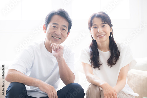 明るい綺麗なリビングでソファに座る 50代夫婦のカメラ目線のクローズアップ