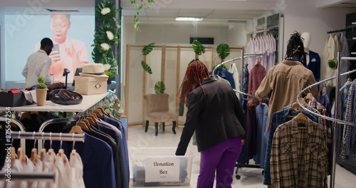 African american clients in fashion boutique donating their clothes for good cause. Customers placing garments in donation box, doing philanthropy gesture in clothing store