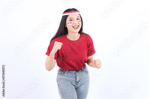 Young Asian woman clenched both fist to celebrate Indonesia independence day on August 17, looking at camera with confident and excited expression wearing red top and flag headband