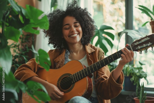 A delighted African teen girl sits with a guitar, playing happily and enjoying a musical moment indoors.