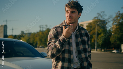 Caucasian smiling man driver recording voice message on mobile phone modern luxury auto background happy male businessman guy record voicemail on speakerphone near car traveling by automobile vehicle