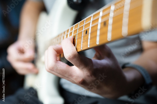 Close up of a man’s left hand and finger on natural brown wooden neck of white electric guitar practicing arpeggio solo