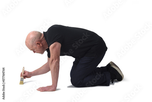 side of a man on knees painting on the floor with a brush on white background