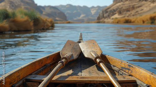 A wooden boat with oars on a calm river through a canyon.