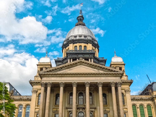 Front Views of the Illinois State Capitol Building in Springfield, IL, USA. Cloudy blue skies overhead. Scaffolding and construction equipment with ongoing construction on the building.