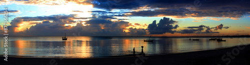 A bright and colorful panorama of sunset on the ocean in Bagamoyo. Silhouette of people and local boats.