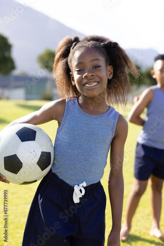 Portrait of happy african american schoolgirl holding football on field at school