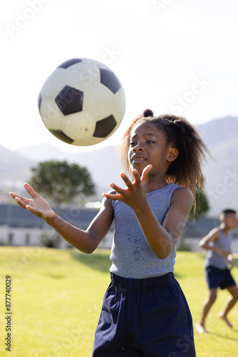 Happy african american schoolgirl playing football on field at school