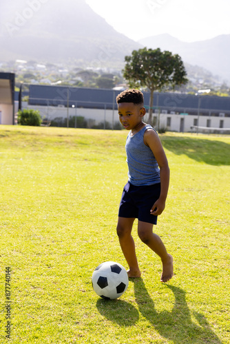 Happy african american schoolboy playing football on field at school