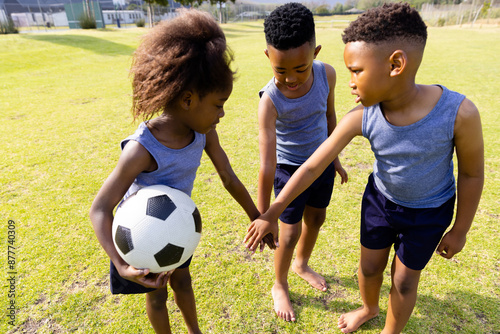 Happy african american schoolchildren playing football on field at school