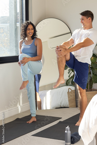 Practicing yoga together, young couple stretching on yoga mats in bedroom