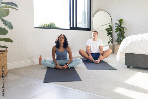 Practicing yoga together, young couple sitting on mats in bedroom, copy space