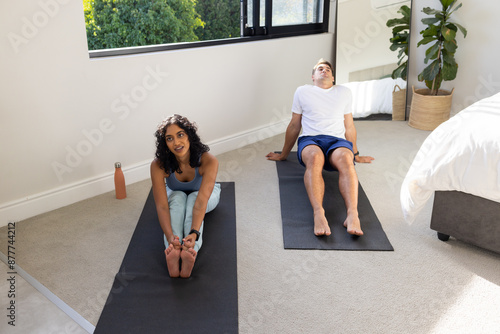 Practicing yoga, young couple stretching on yoga mats in bedroom