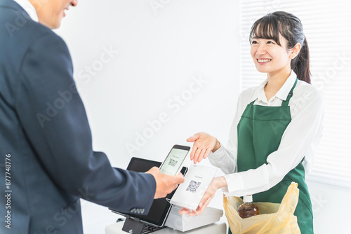 コンビニでスマホ・QRコード決済を案内する女性店員と買い物客のサラリーマン男性 