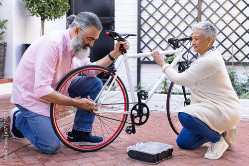 Repairing bicycle together, senior couple enjoying outdoor activity in courtyard