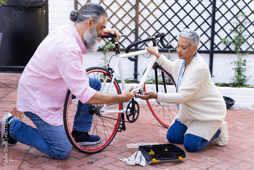 Repairing bicycle together, senior couple working with tools in backyard