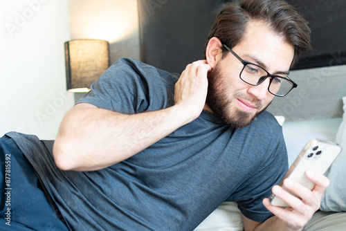 Hombre con dolor de cuello reposa en su habitación. Joven apuesto acostado usando el teléfono celular