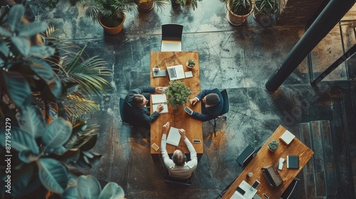 The photo shows a group of diverse professionals in a modern office setting. They are gathered around a table, working on a project together. The office is bright and airy, with lots of plants and