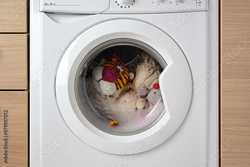 Close-up a white washing machine washes many dirty children's toys.