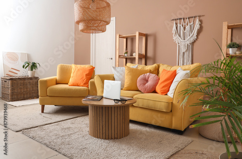 Interior of living room with yellow sofa, armchair and laptop on wooden table