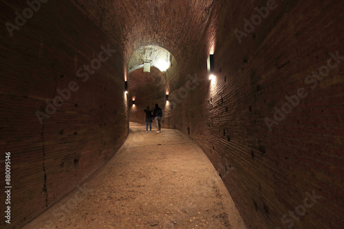 Castel Sant'Angelo, Rome, Italy - December 10, 2023: Indoor and low angle view of a couple tourist walking on corridor in the arch tunnel with stone walls 