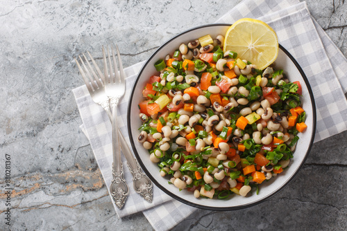 Delicious salad with black-eyed beans, carrots, onions, tomatoes, basil, parsley dressed with olive oil and lemon juice closeup on the plate on the table. Horizontal top view from above