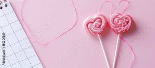 Valentine's Day theme with light pink background, featuring two heart-shaped lollipops or candy on sticks, a calendar, and empty space for text or images.