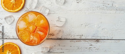 Top view of a refreshing orange summer drink with ice on a white wooden surface with a blank area for text or images.