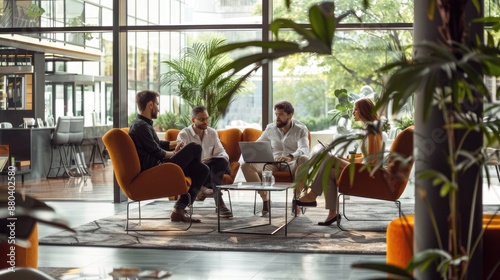 Three business people having informal meeting in modern office space with big windows and green plants.