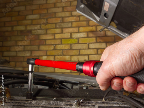 Closeup of a man’s hand in the engine bay of a car in a garage, turning a torque wrench tool on a nut or bolt, to tighten to the correct tension.